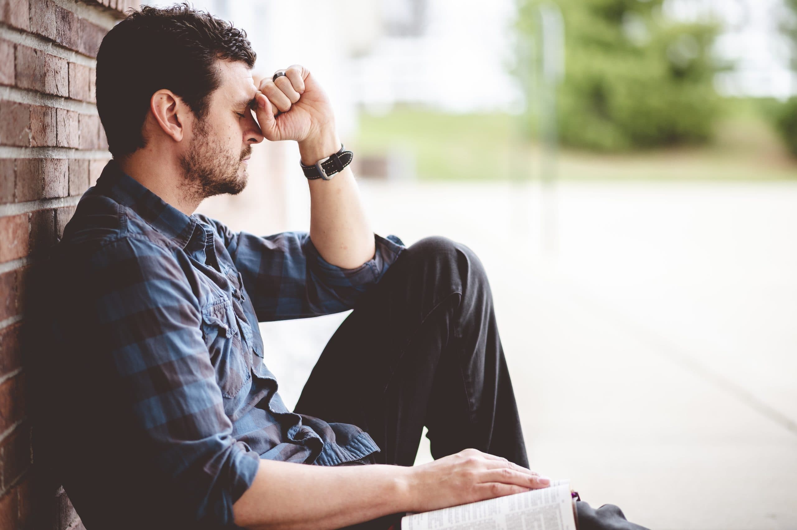 10 Common Mental Health Issues - A lonely person sitting near a brick wall with the Bible on his lap