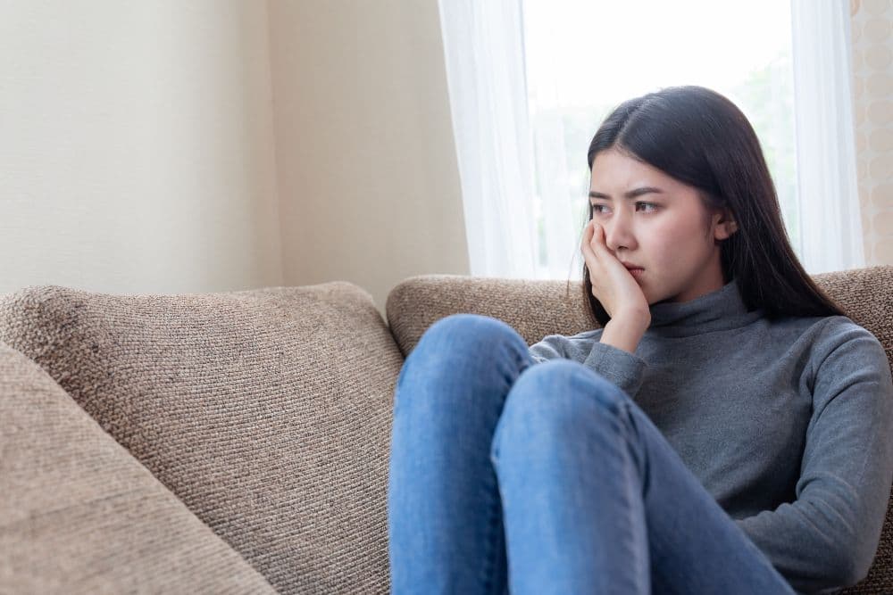 A person looking sad, sitting on a couch, and thinking about searching for inspirational happiness quotes for tough days.