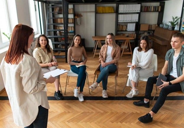A support group of five people, engaged in a therapist-led discussion.