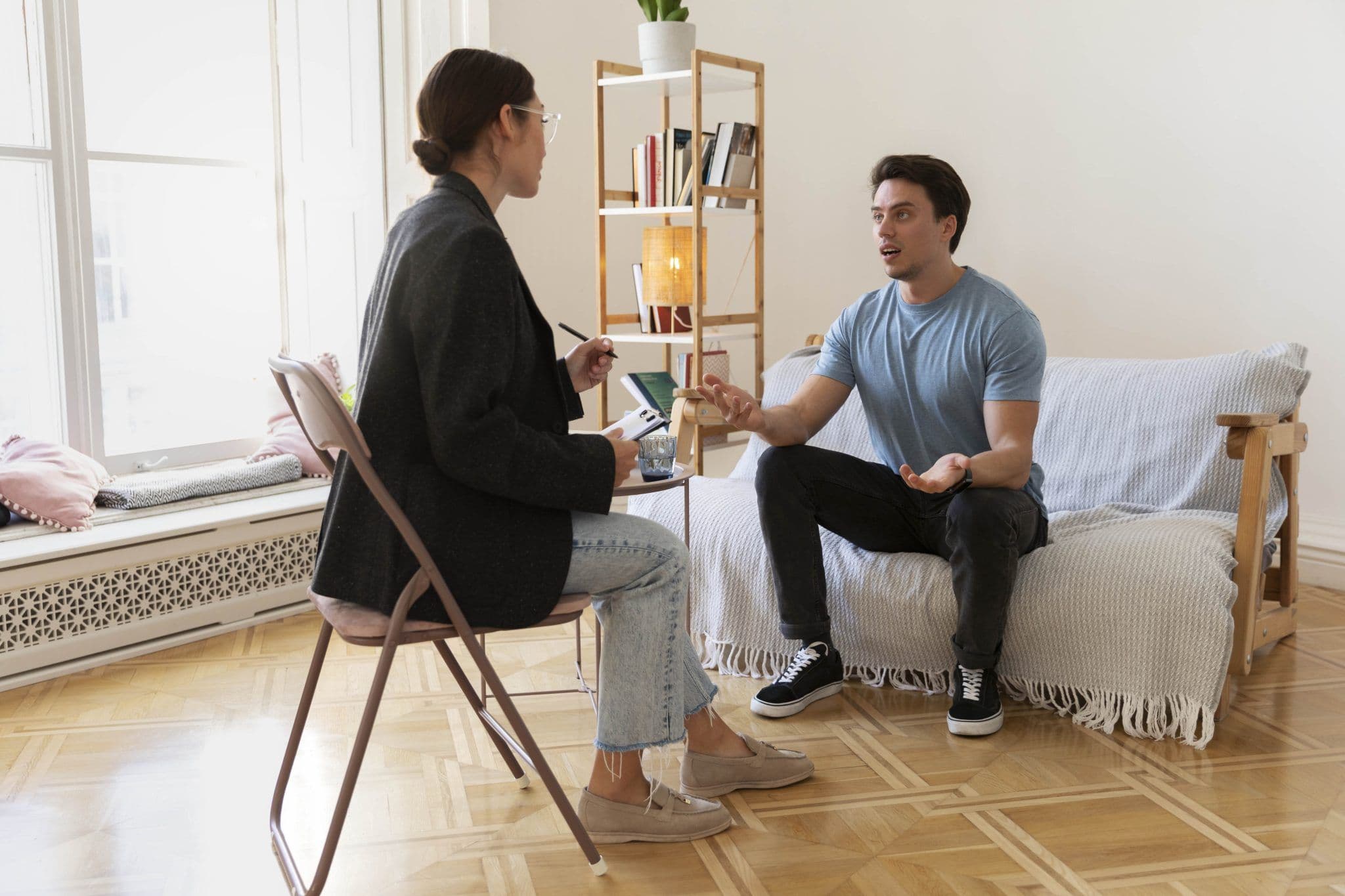 A client sitting on a sofa opposite to the therapist who is sitting in a chair. The client asks questions to determine the right Therapist in Singapore for their needs.